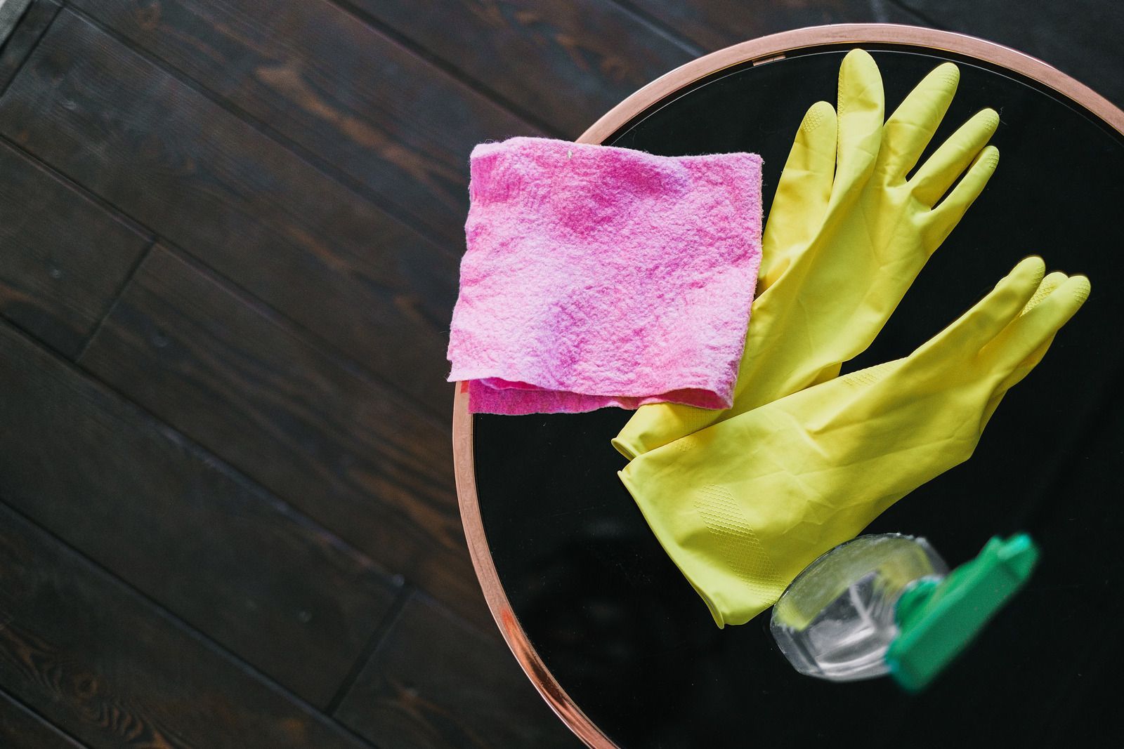 A pair of yellow rubber gloves and a pink cloth are on a table.
