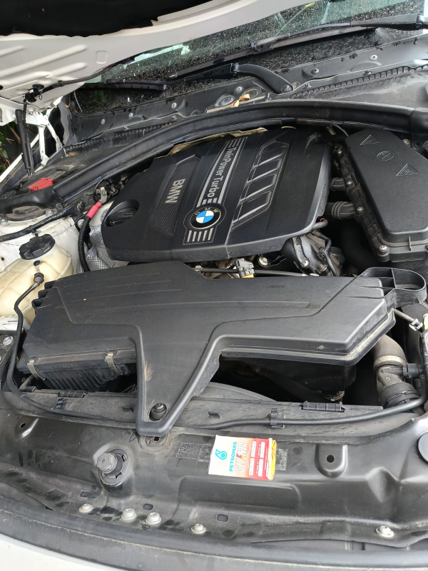 Il vano motore di un'auto BMW, caratterizzato da una copertura motore nera con il logo BMW e da un sistema di aspirazione dell'aria a vista.