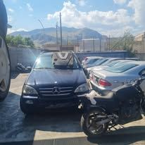 Un SUV Mercedes di colore scuro parcheggiato all'aperto, con una motocicletta in primo piano e altre auto nelle vicinanze.