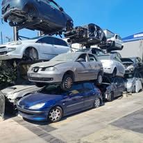 Un mucchio di veicoli recuperati e accatastati in una discarica a cielo aperto, sotto un cielo azzurro e limpido.