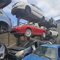 In una discarica, una pila di automobili mostra un veicolo rosso al centro e altre auto in vari stadi di smontaggio.