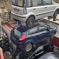 In una discarica, tre auto sono ammassate, con una vettura argentata precariamente in bilico sopra una berlina blu.