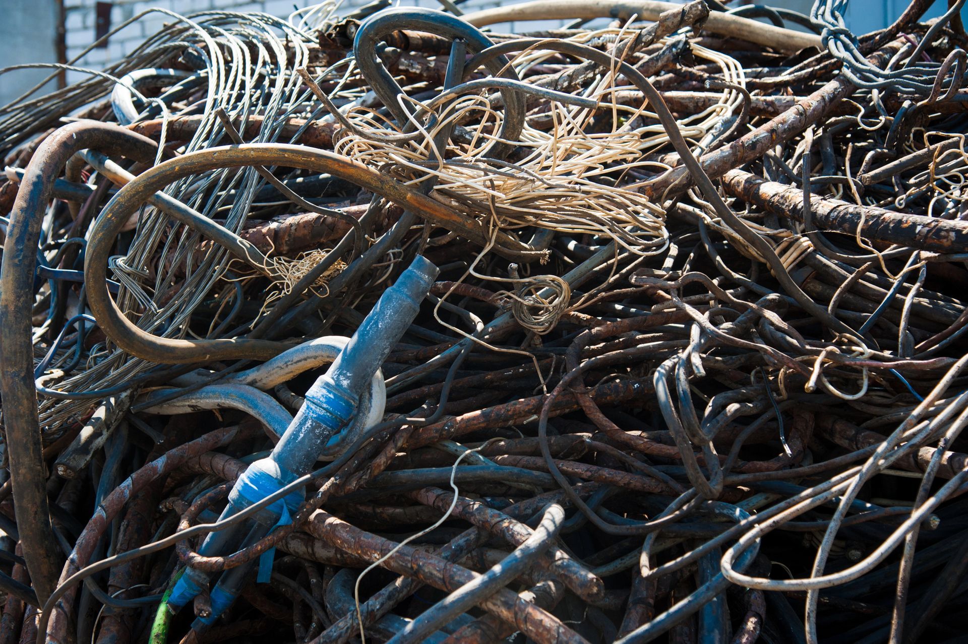 Un grande e disordinato ammasso di fili e cavi metallici arrugginiti e aggrovigliati, con un connettore di plastica blu ben visibile in primo piano.