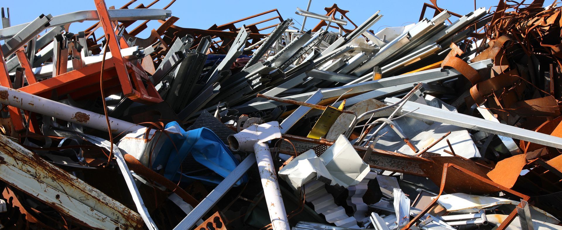 Un grande cumulo di rottami metallici di vario genere, tra cui travi arrugginite e parti in acciaio, stagliarsi contro un cielo azzurro e limpido.