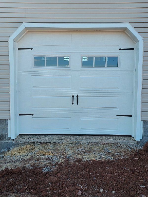 White garage door with black hardware and windows, set in a white frame, in front of a building with beige siding.