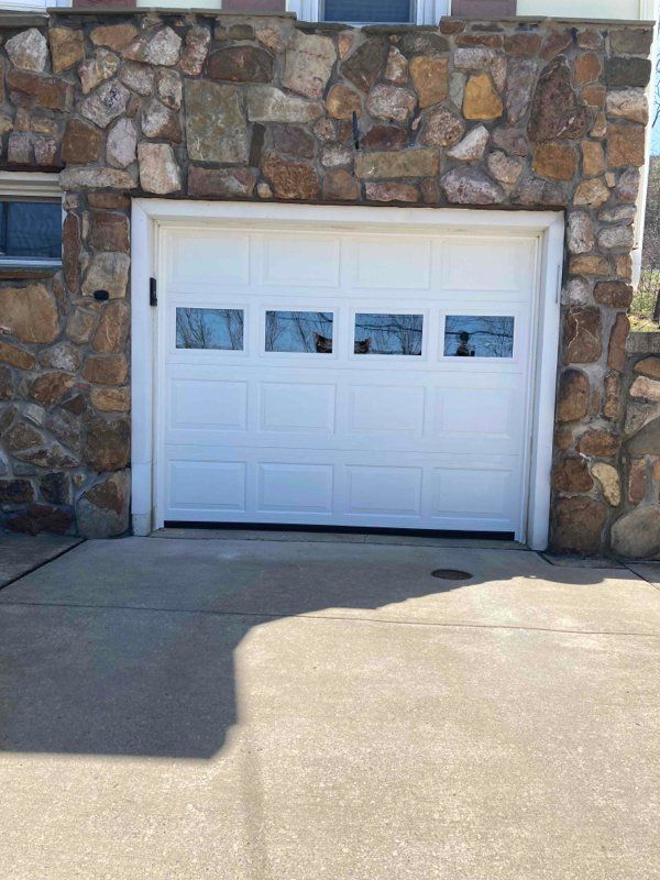 White garage door with four window panels, set in a stone facade. Concrete driveway in front.