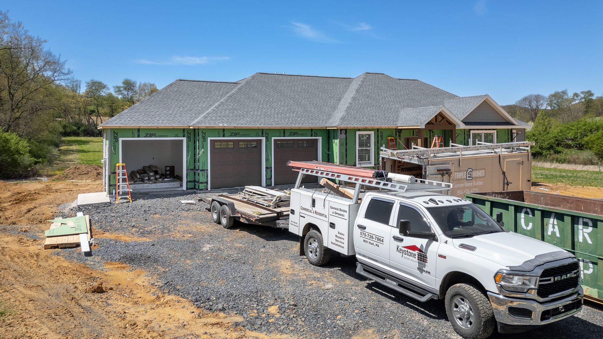 Construction site with a white work truck towing a trailer in front of a house with a gray roof.
