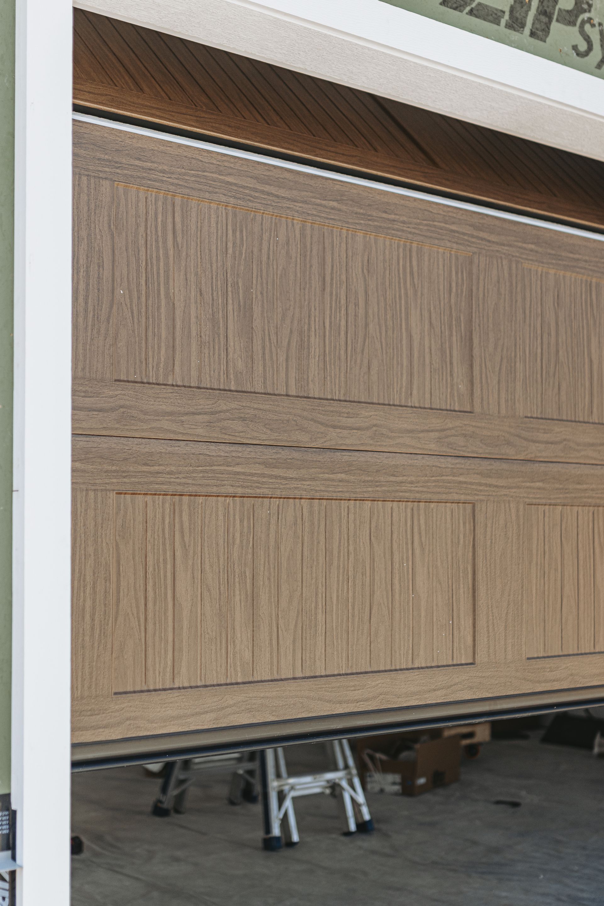 Garage door with wooden texture, partially open, revealing a garage interior with a stepladder and other items.
