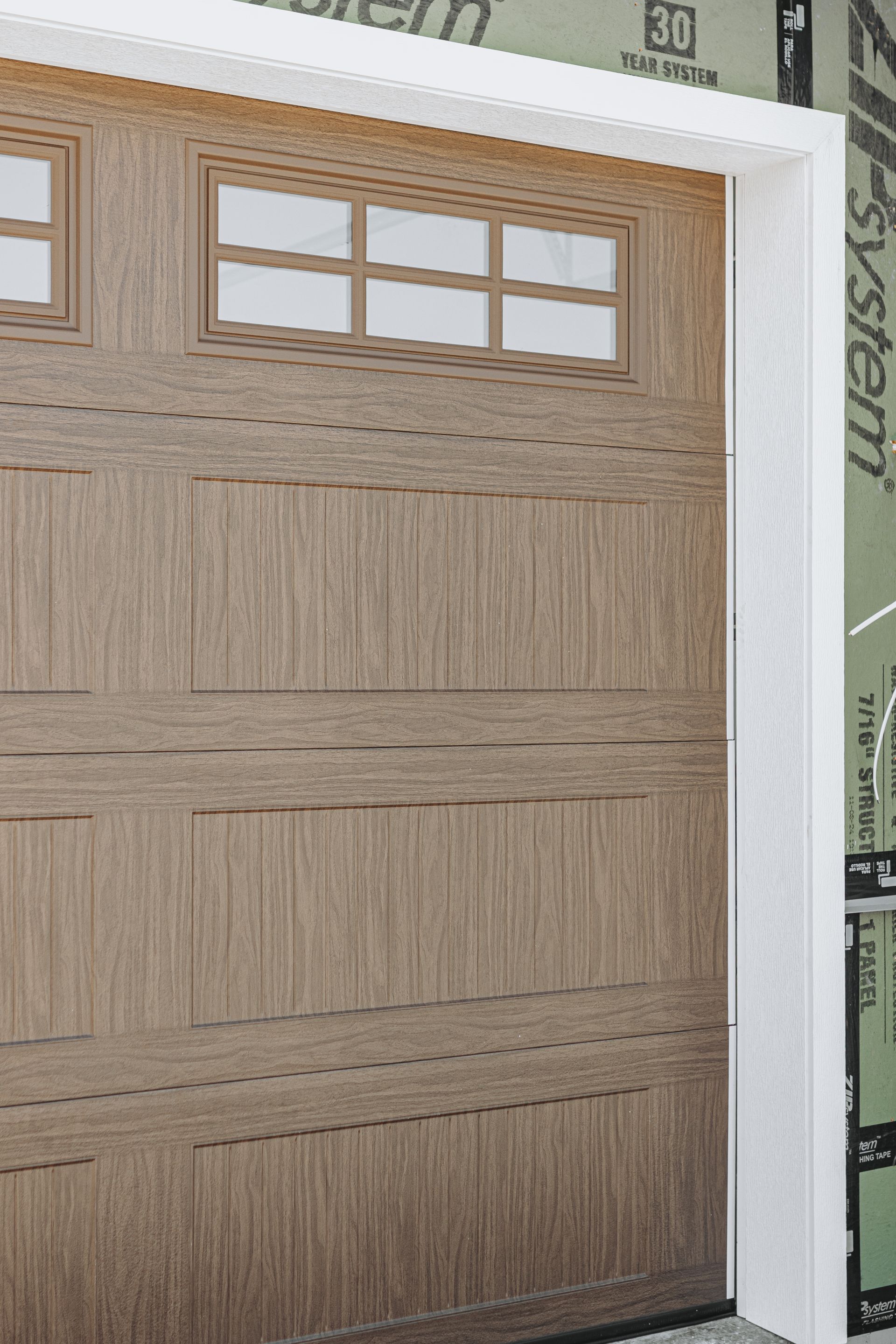 Close-up of a brown wooden garage door with rectangular panels. A white trim frames the door and a window section.