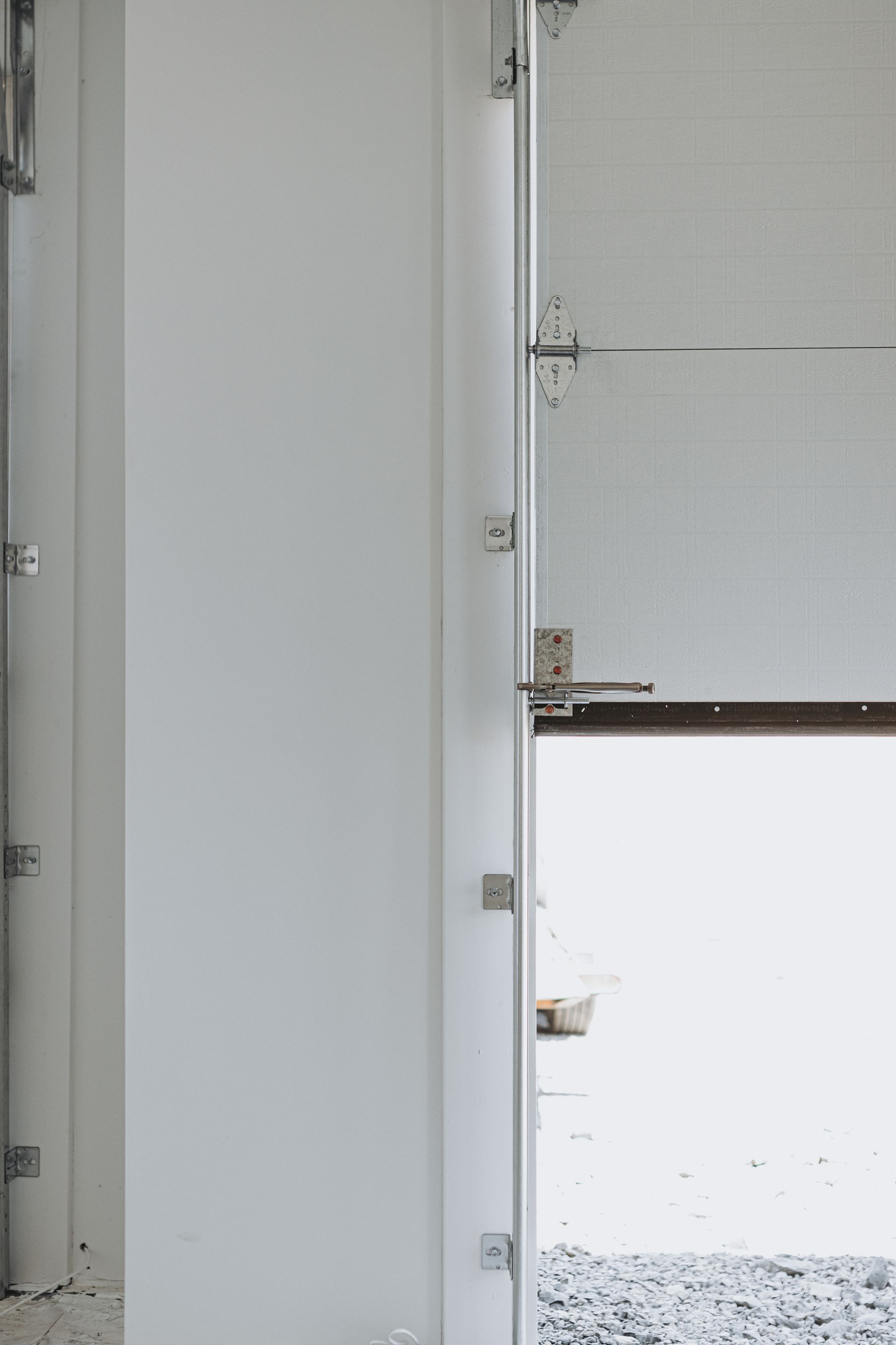 Close-up of a partially open, light-colored door. White pillar on the left, metal support and opening to exterior on the right.