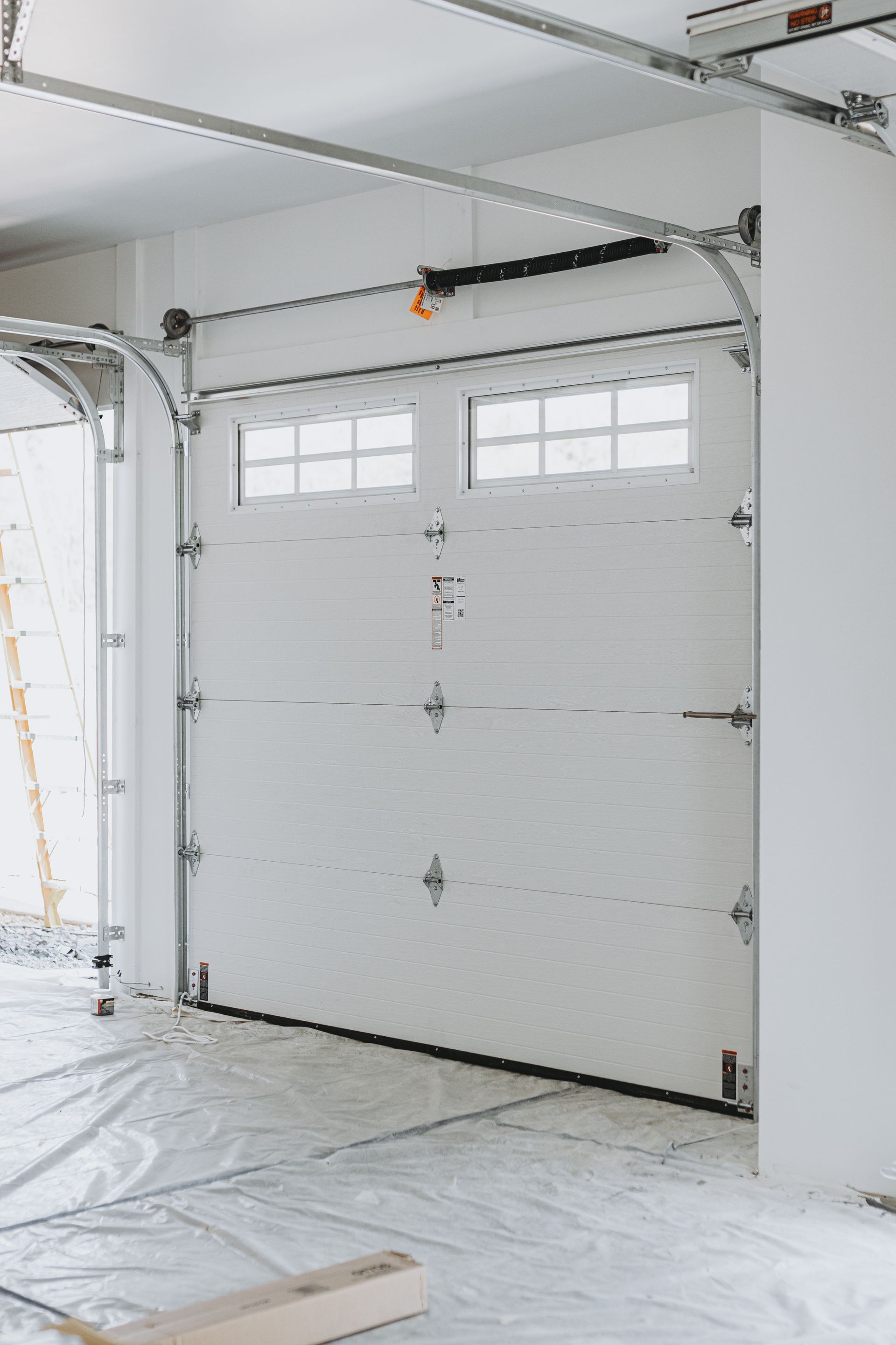 White garage door with windows, inside a room with white walls and protective floor covering.