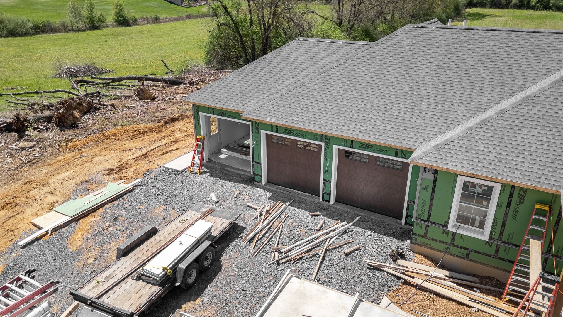 Construction site with a partially built garage. The roof is gray, and the garage doors are brown.