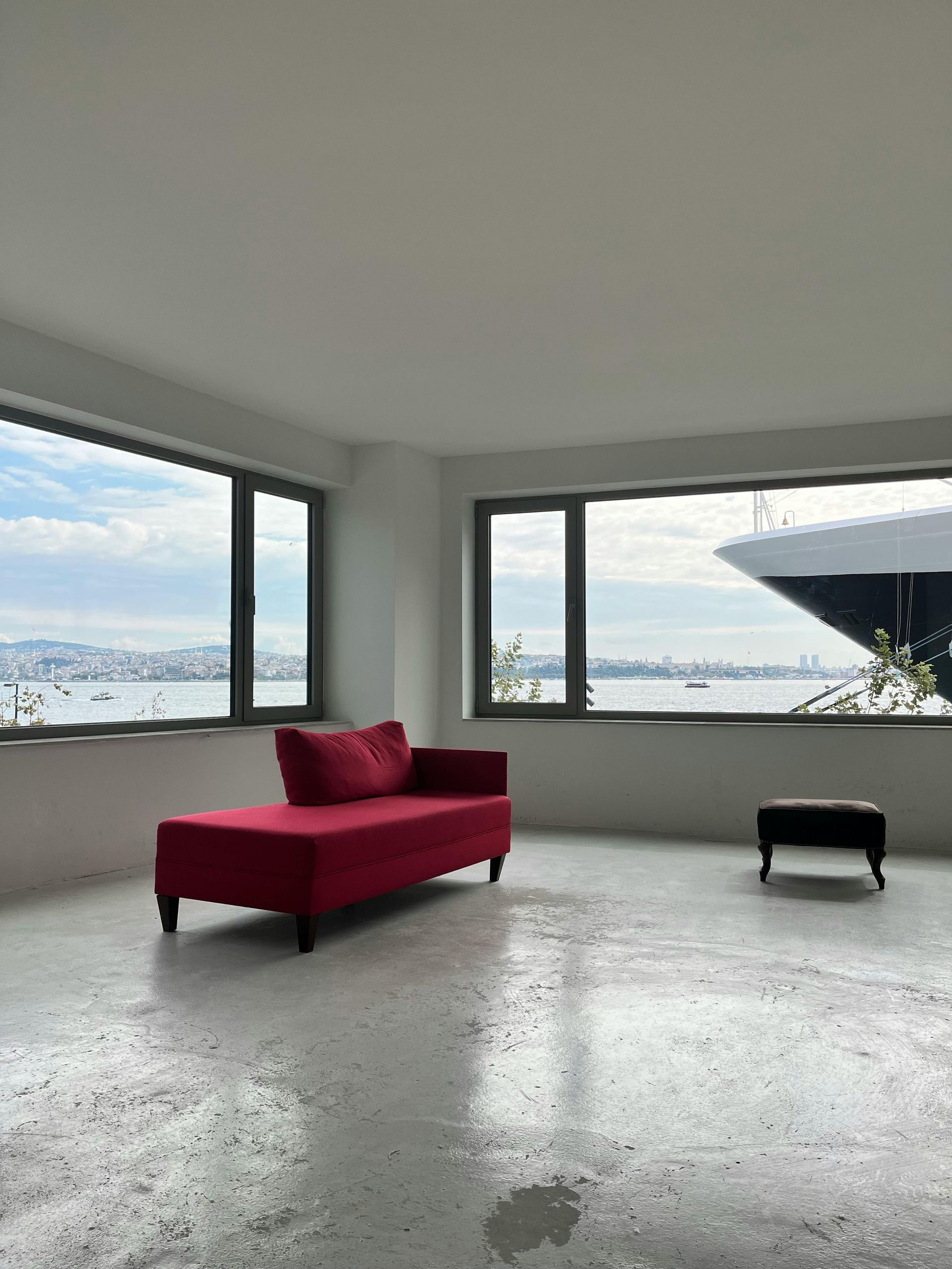 A bright red chaise lounge and black ottoman in a room with a large window overlooking a waterfront.