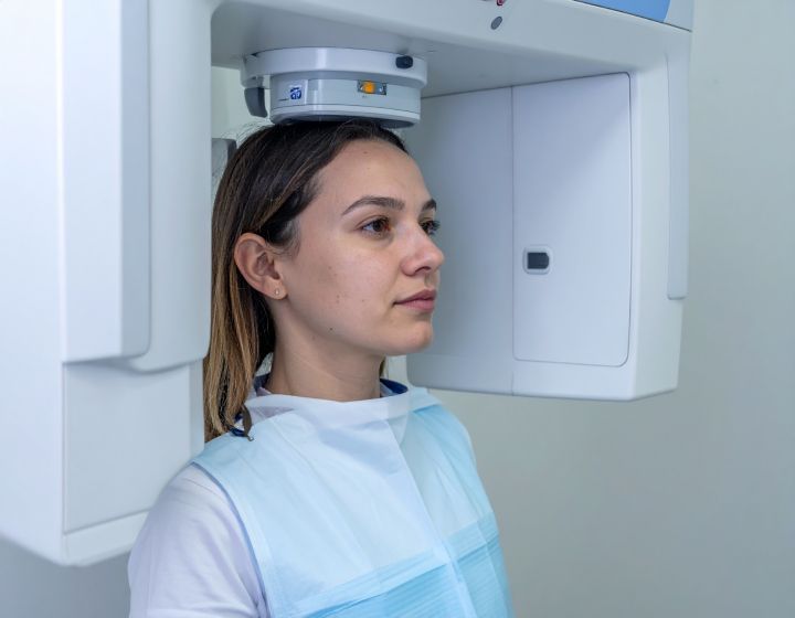 Woman having dental x-ray scan; wearing protective bib, standing in front of the machine.