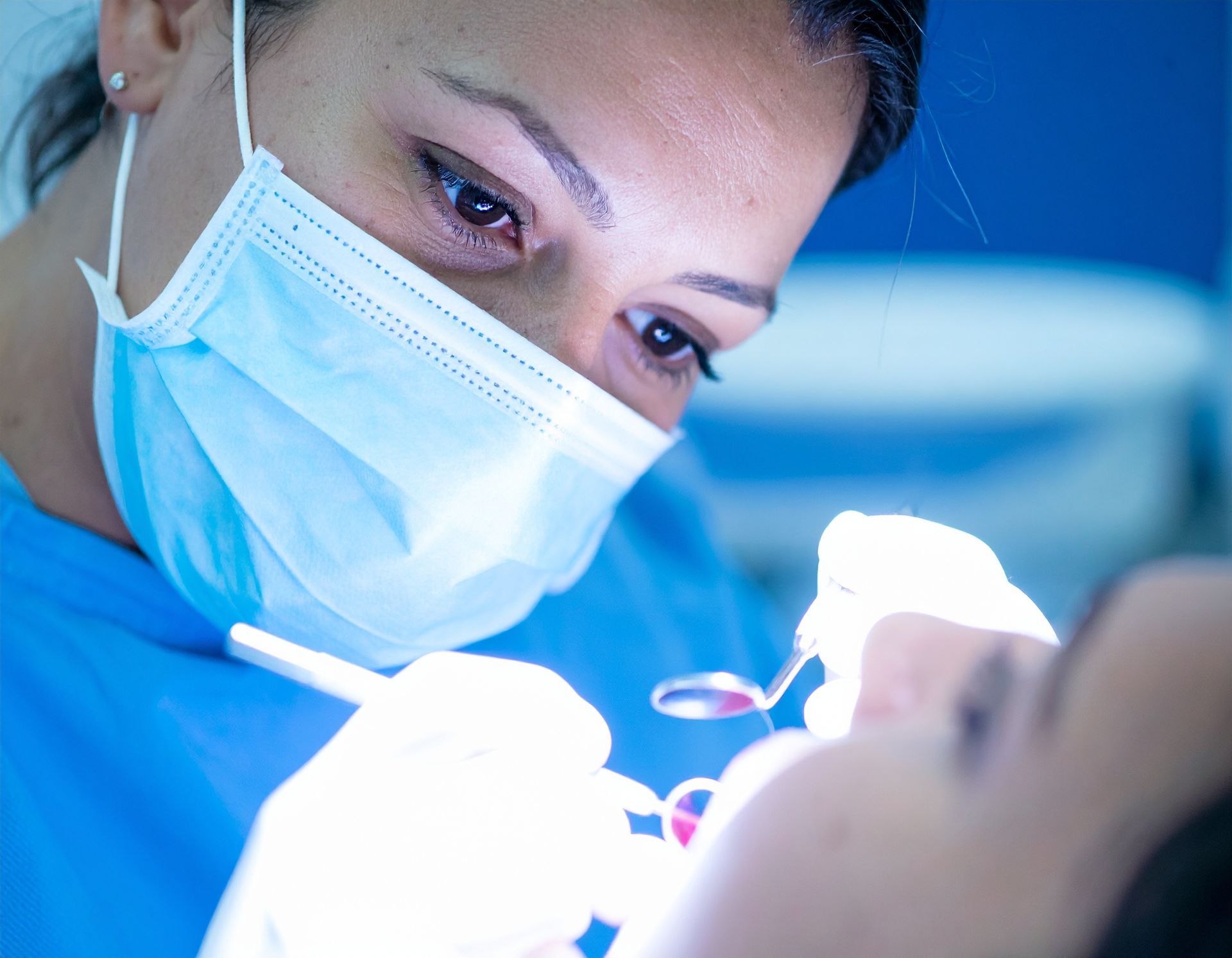Dentist wearing a mask examines a patient during a dental procedure under bright blue light