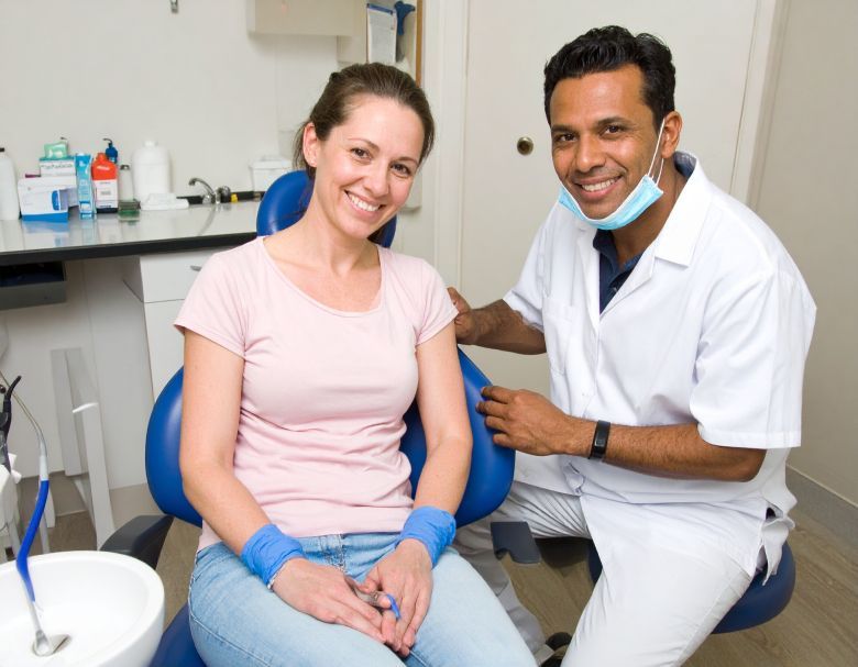 Woman seated in dental chair smiling, dentist in white coat smiles beside her.