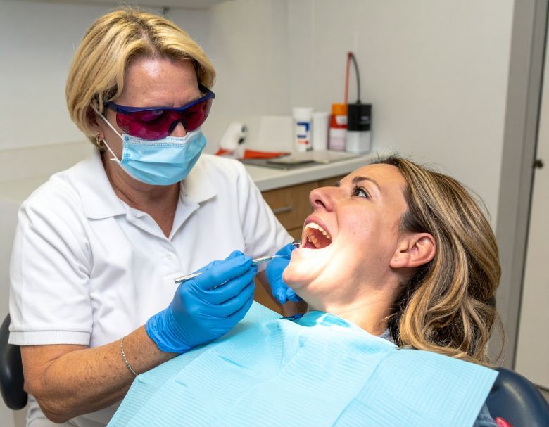 Dentist examining patient's teeth with dental tools in a dental office. Patient's mouth open, dentist wearing protective glasses and mask.