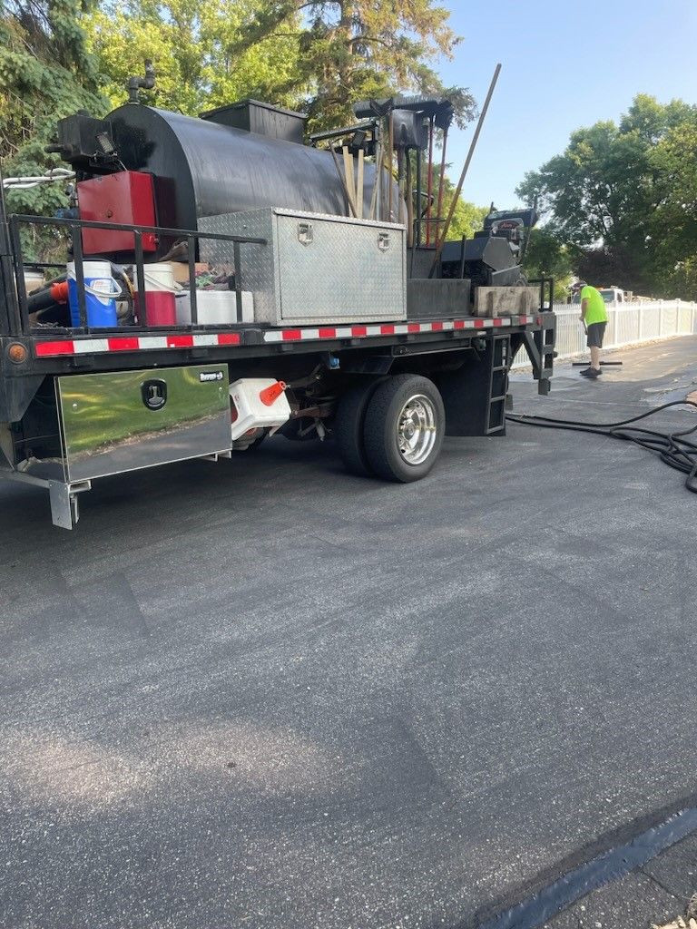 Flatbed truck with equipment parked on a road, with workers and a large hose or cable nearby.