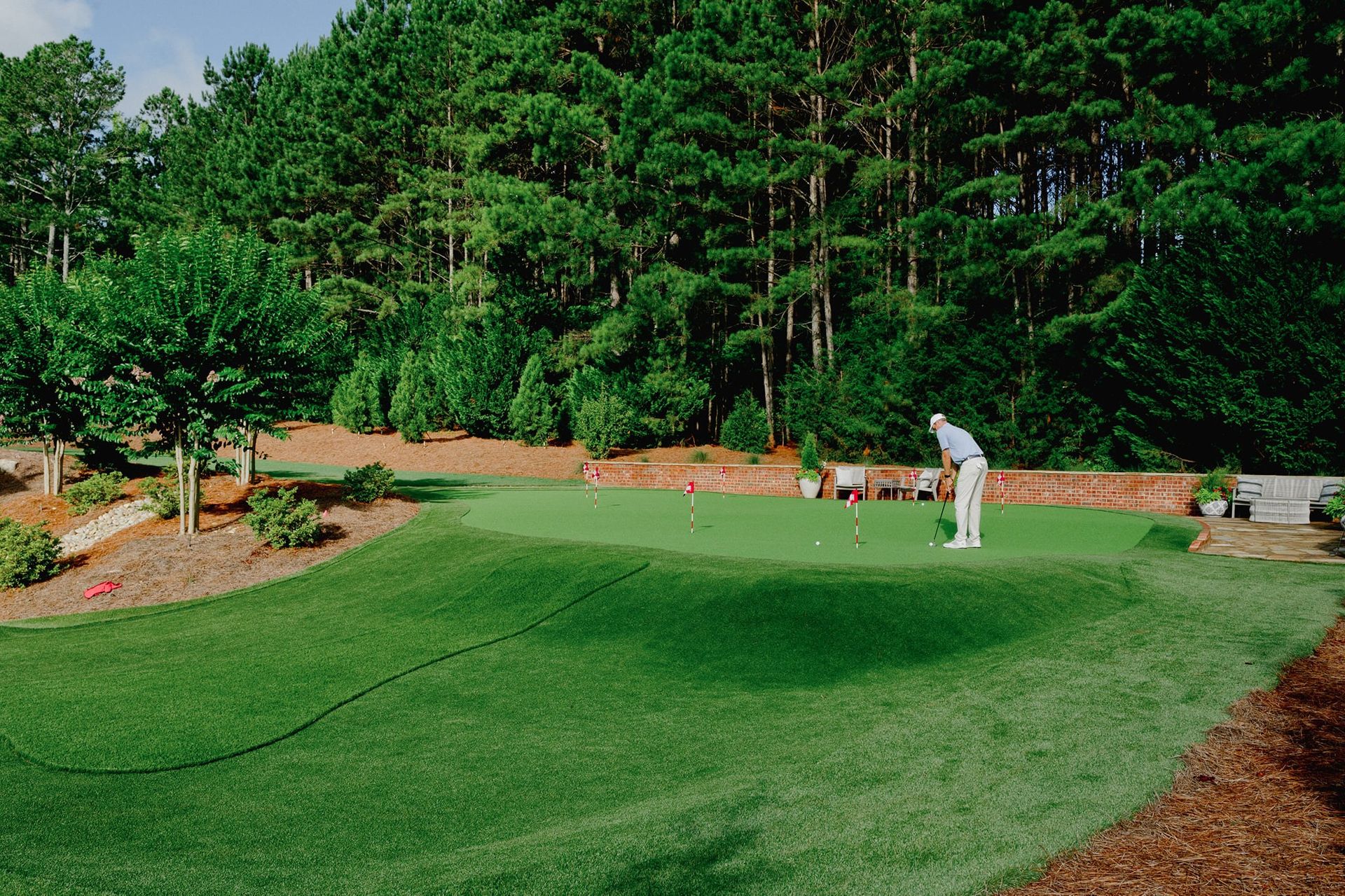 Man putting on a backyard golf green, surrounded by trees and greenery.