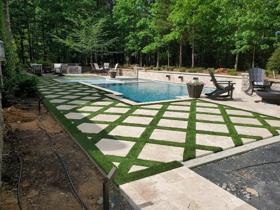 Swimming pool with stone and grass grid pattern; outdoor setting with trees.