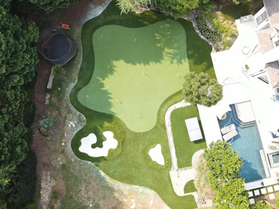 Overhead view of a backyard putting green with a sand trap, swimming pool, and a house.