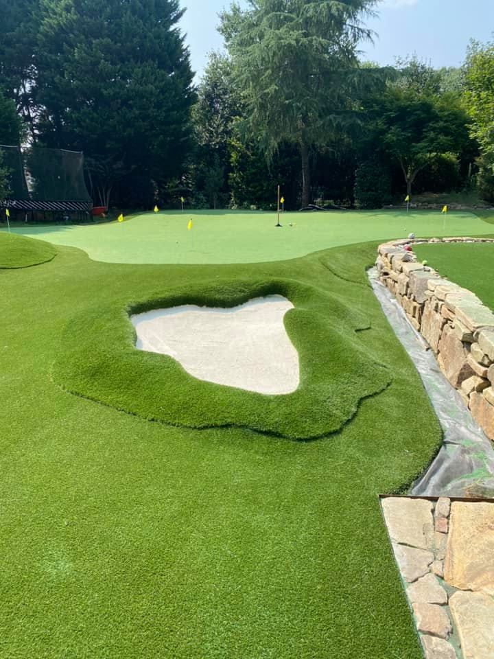 Artificial turf putting green with a sand trap and stone retaining wall.