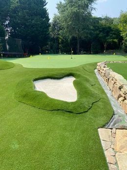 Miniature golf course with green turf, a sand trap, and a stone wall.