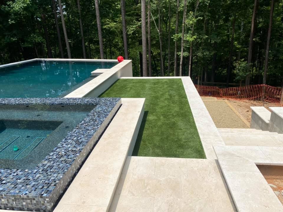 Pool area with pool, hot tub, artificial grass, and forest backdrop.