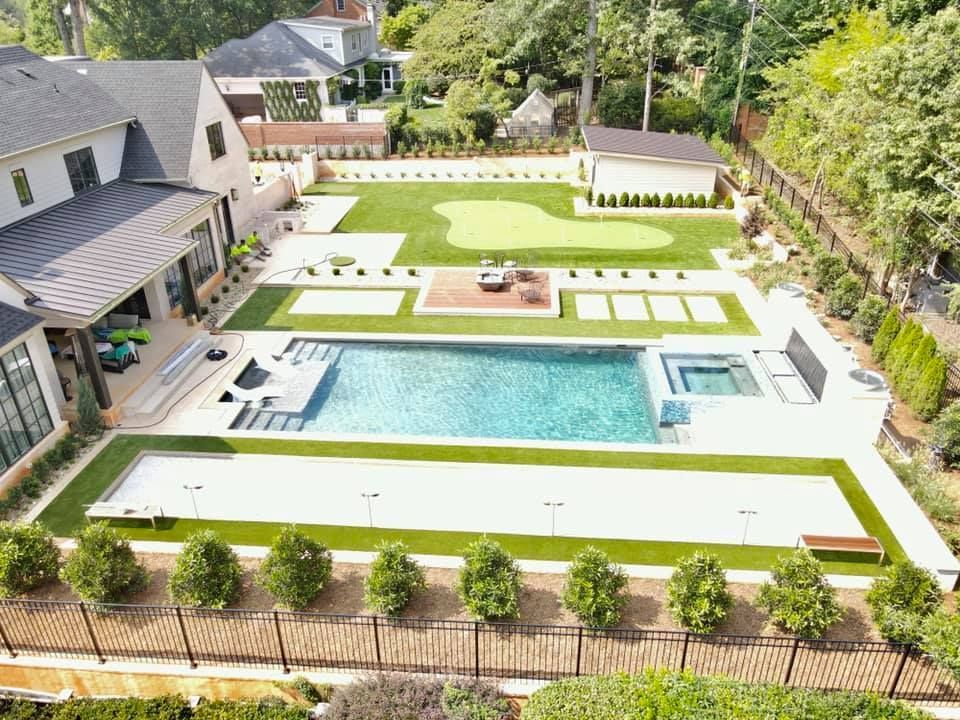 Aerial view of a luxury backyard with a pool, putting green, and a large home.