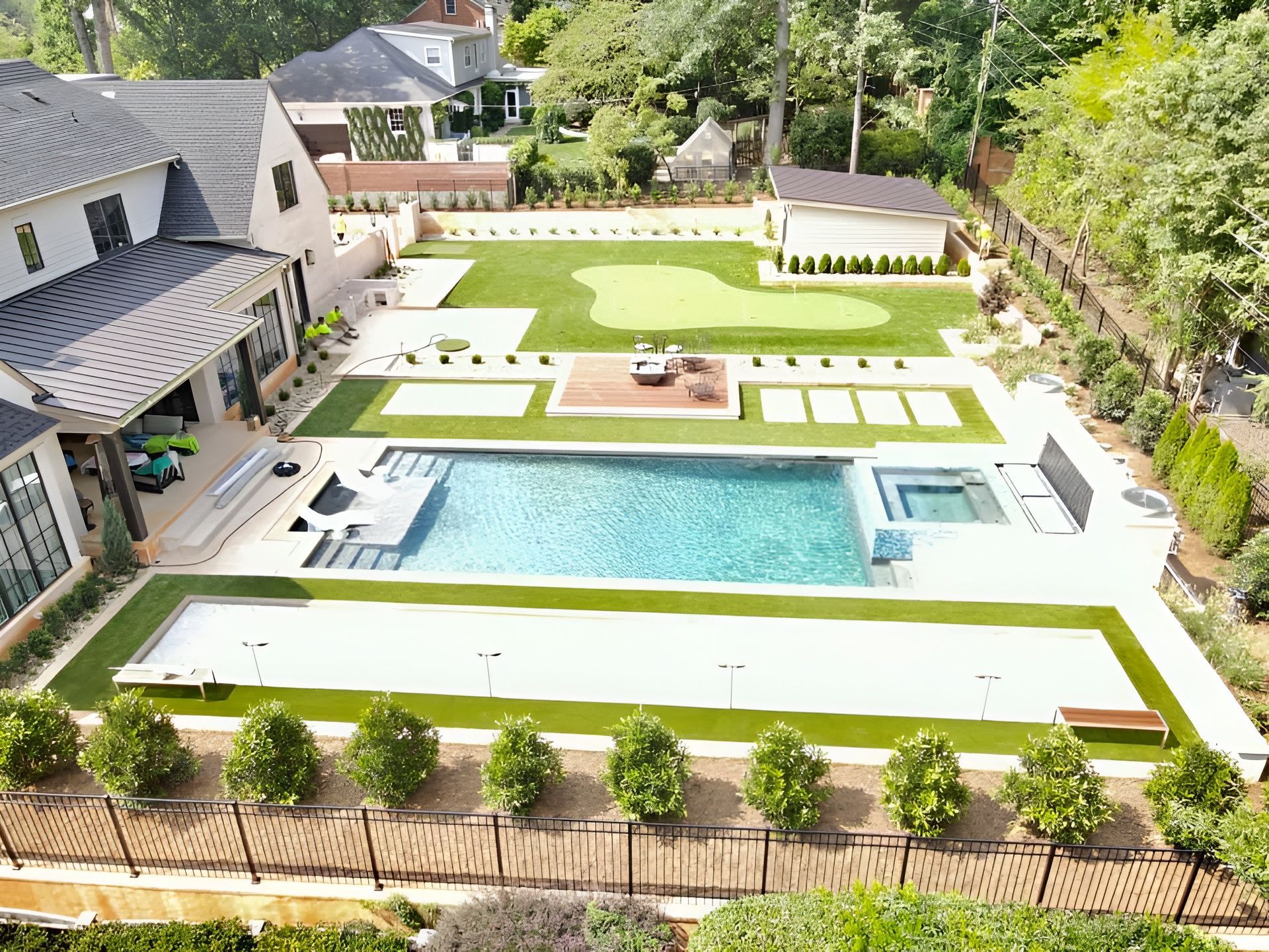 Aerial view of a luxury backyard with a pool, putting green, and manicured landscaping.