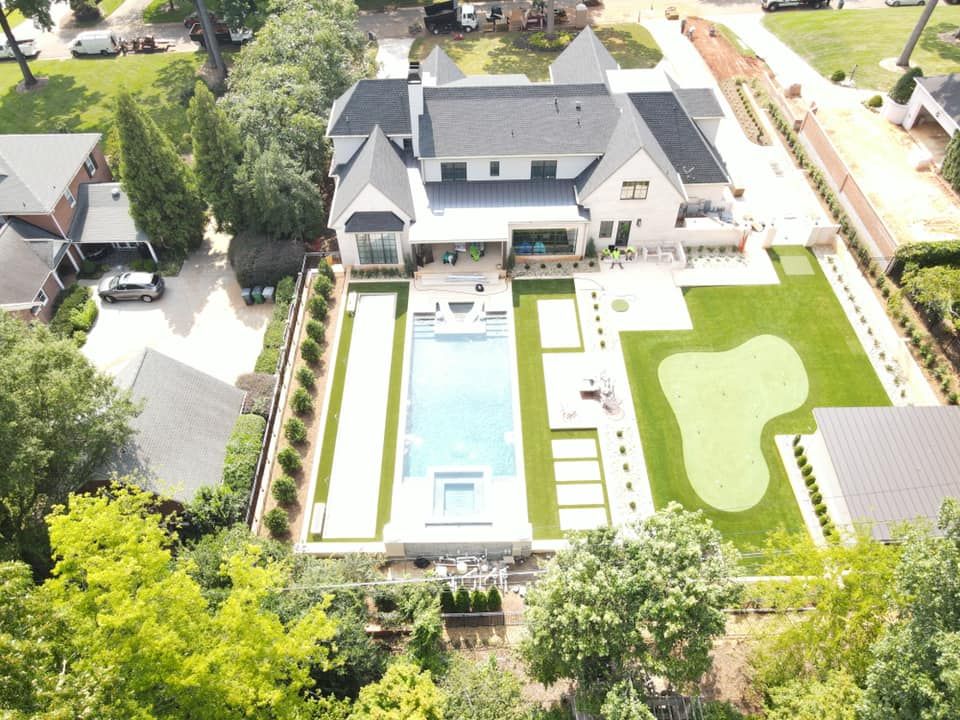 Aerial view of a large modern house with a long pool and putting green.