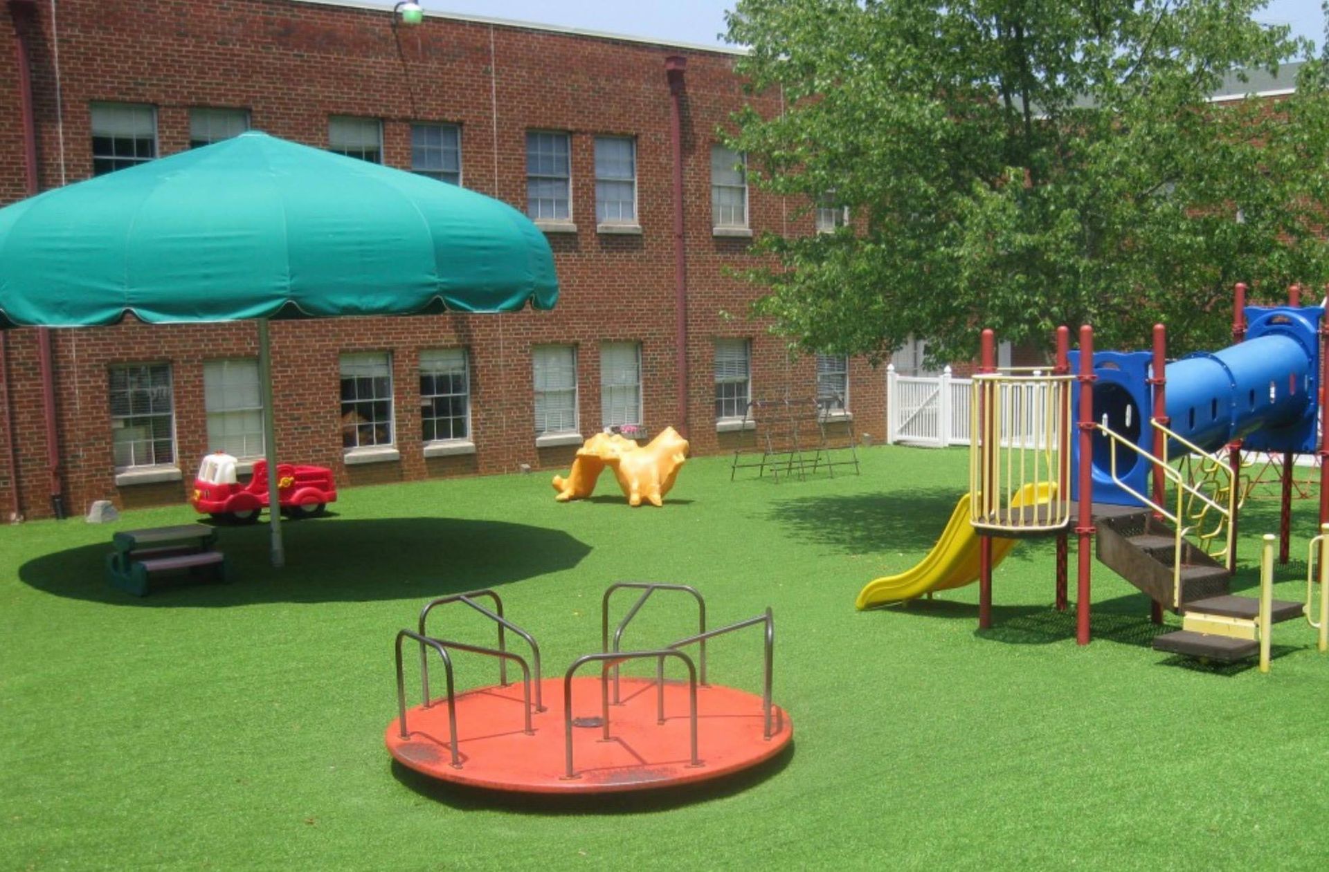Playground with a green canopy, play structures, and a brick building in the background.