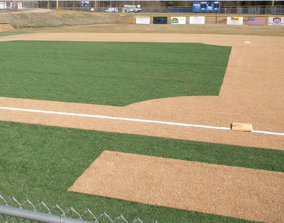 Baseball field with green artificial turf and brown dirt infield.
