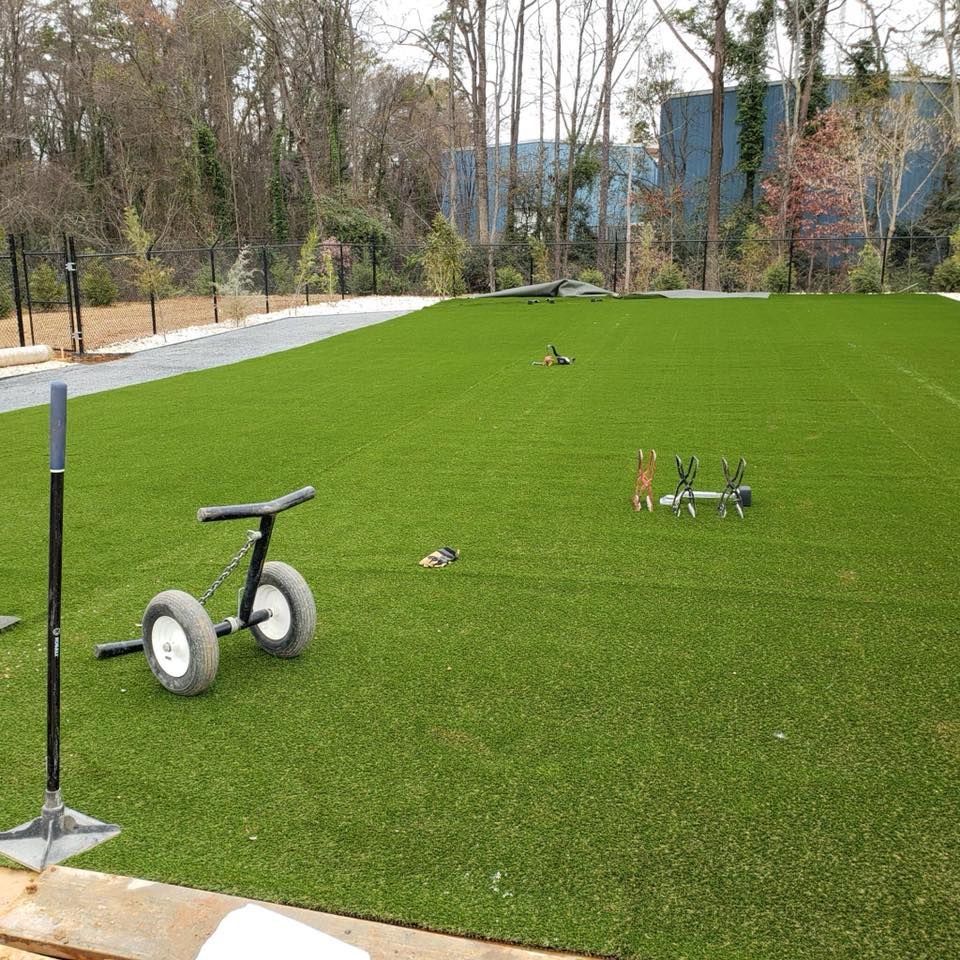 A bright green artificial turf lawn with a wheelbarrow and lawn games set up outdoors.