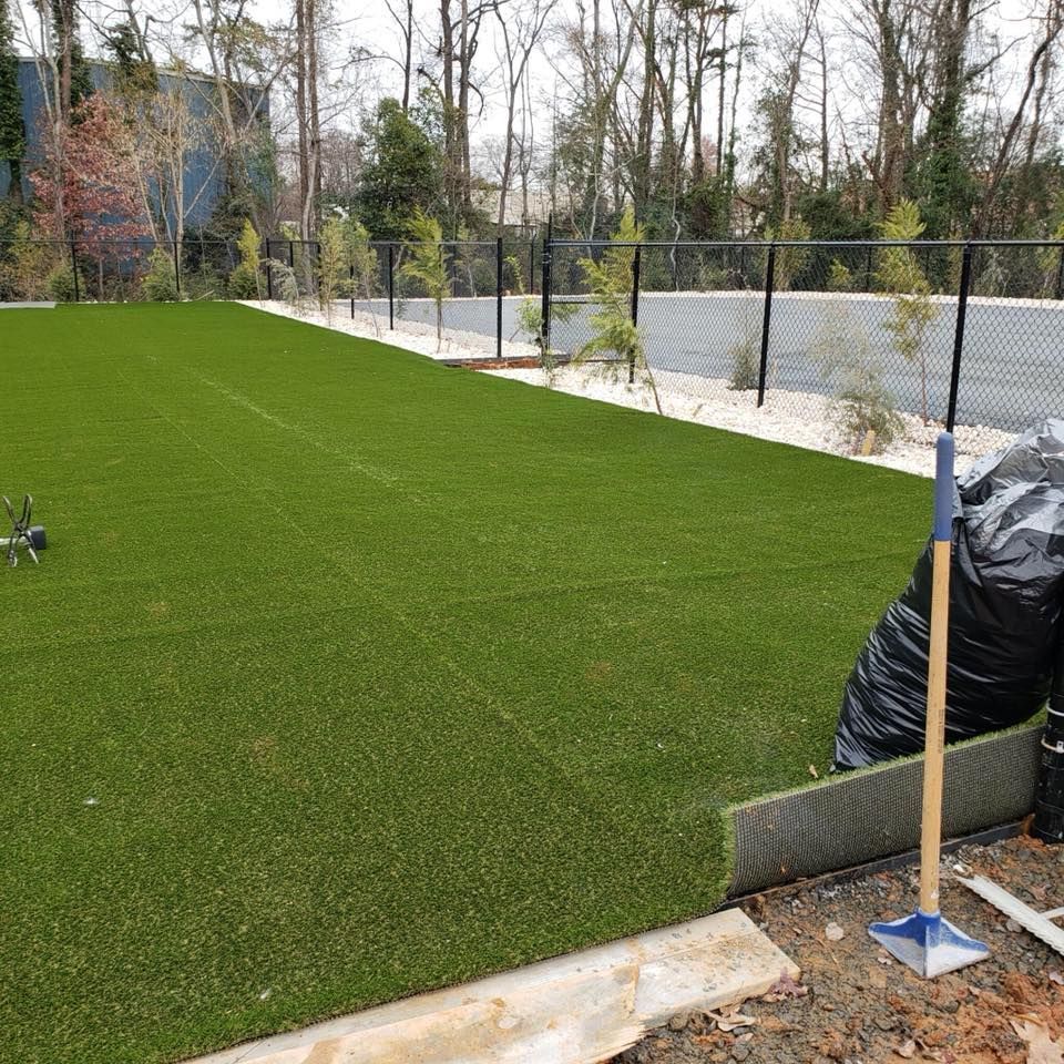 Artificial turf installation: Green field, black fence, shovel, and tools on the edge.