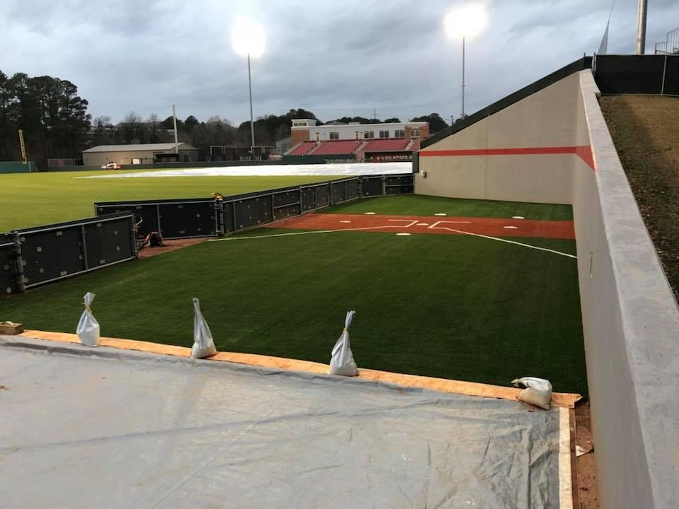 Baseball field with green grass, orange dirt, under overcast sky.