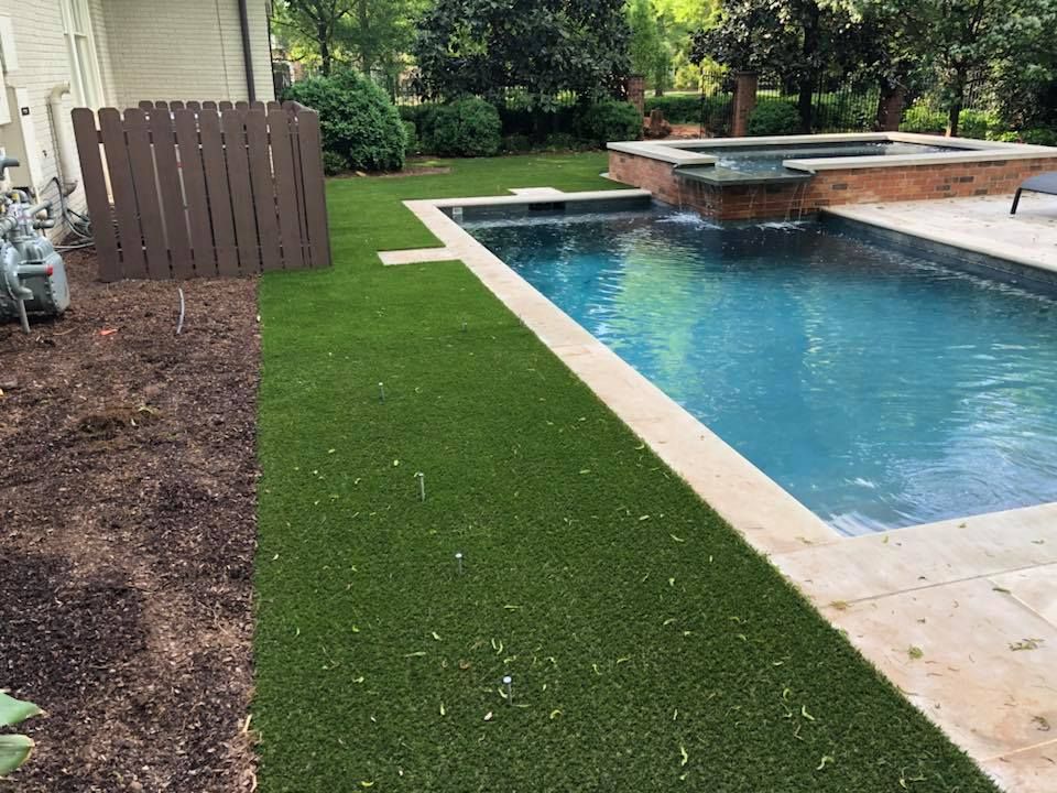Backyard with a pool and artificial grass. Brown fence on the left, with green grass and pool.