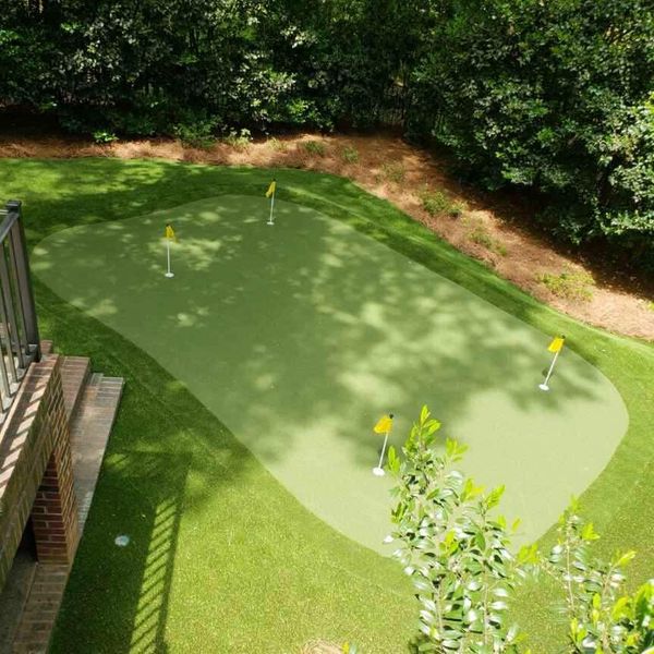 Backyard putting green with four yellow flags, surrounded by grass and trees.