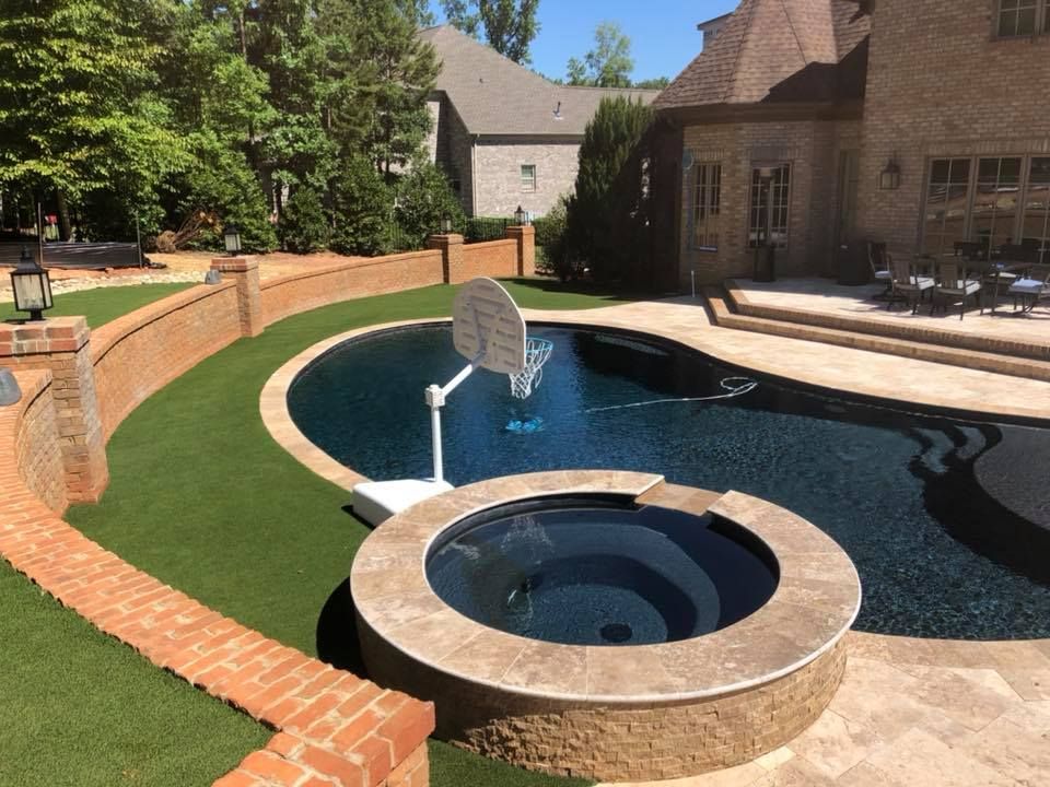 Luxurious backyard with a pool, spa, basketball hoop, and brickwork.