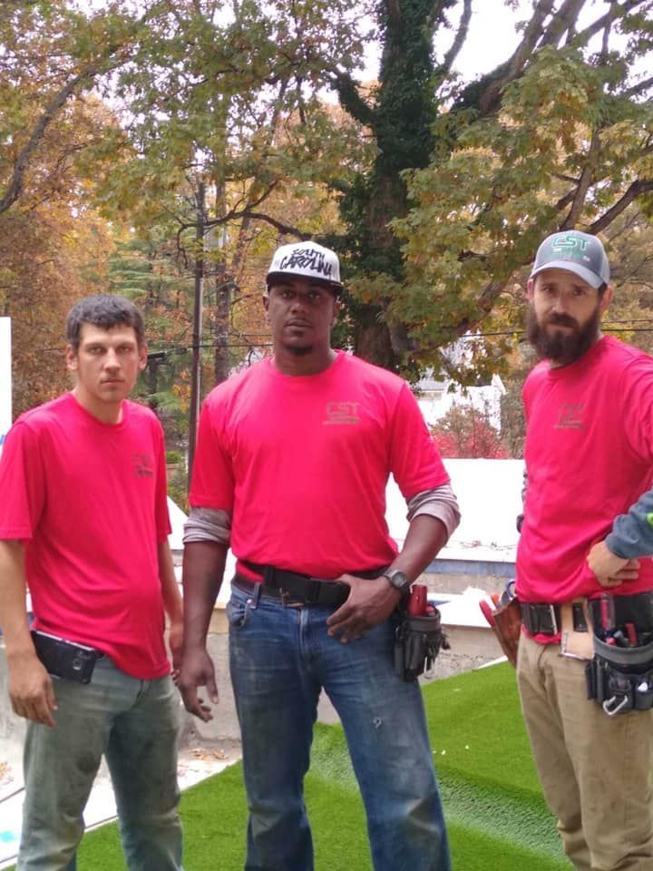 Three construction workers in red shirts, posed outdoors on turf, tools visible.