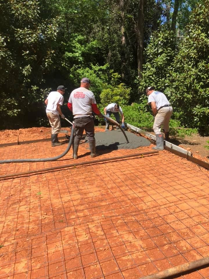Workers pouring concrete onto a rebar grid outdoors, surrounded by trees.