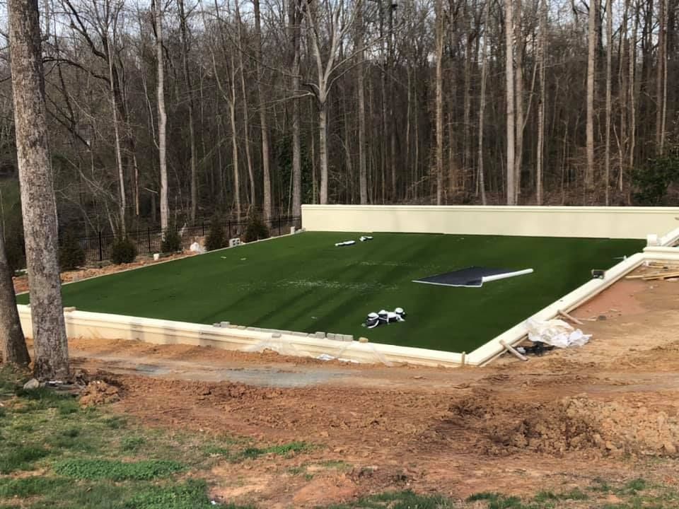 Artificial turf installed in a backyard, surrounded by retaining wall and trees.