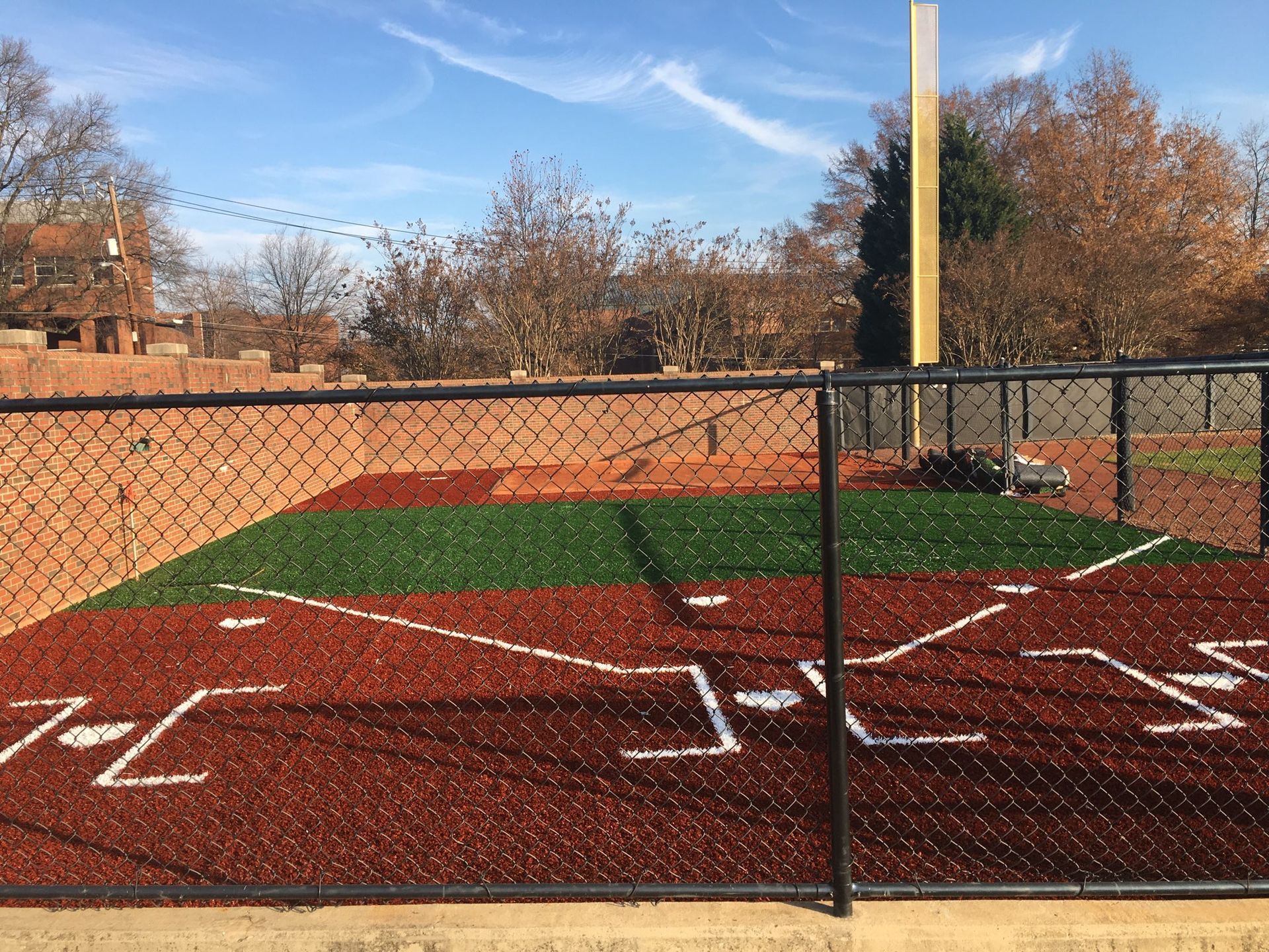 Baseball infield with brown dirt, green grass, and white lines, behind a black fence.