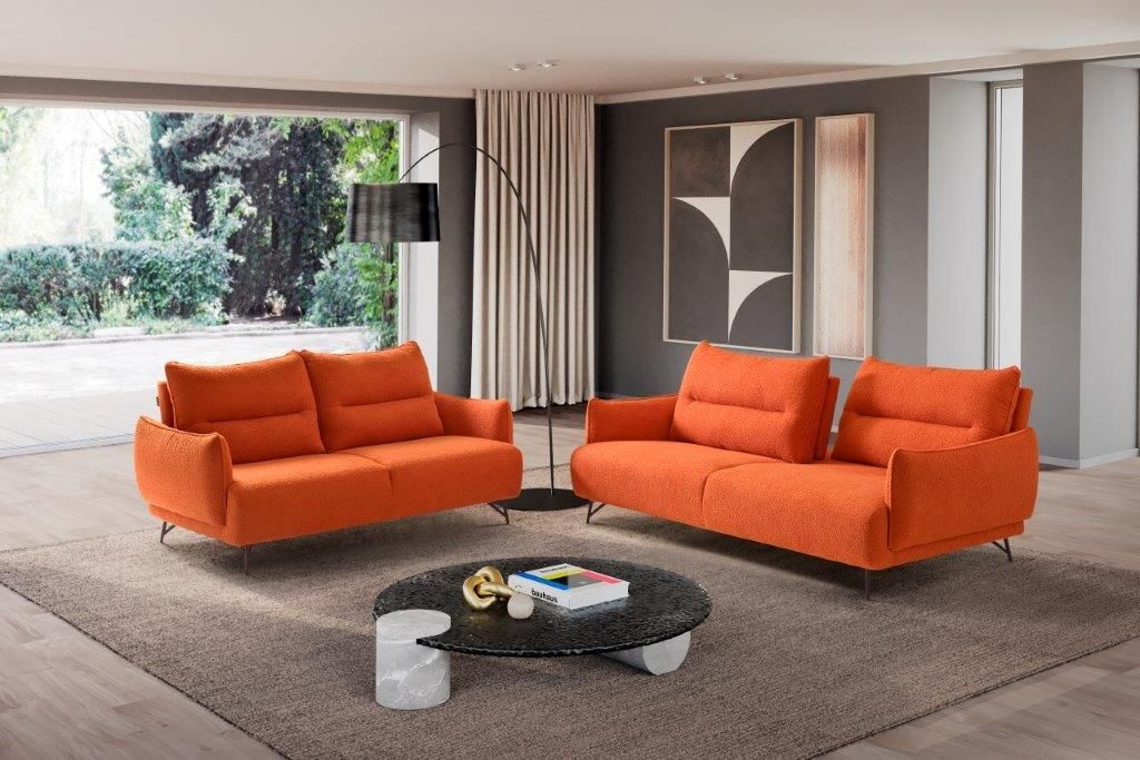 Due divani arancioni in un soggiorno moderno con un tavolino rotondo e opere d'arte astratte.