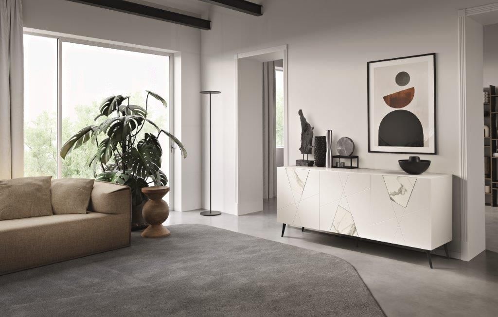 Soggiorno con divano beige, grande finestra, opere d'arte astratte e un mobile bianco con elementi decorativi.