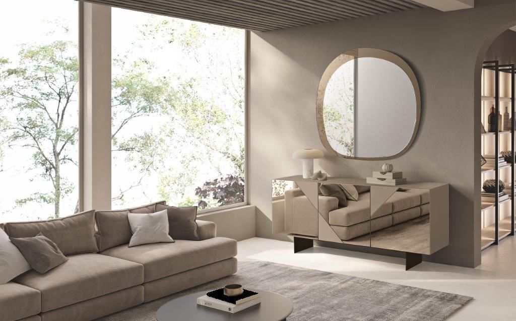 Soggiorno con divano componibile beige, ampie finestre e una credenza con specchio rotondo.