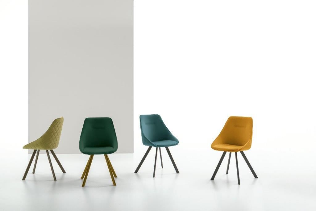 Quattro sedie da pranzo colorate con gambe affusolate su uno sfondo bianco.