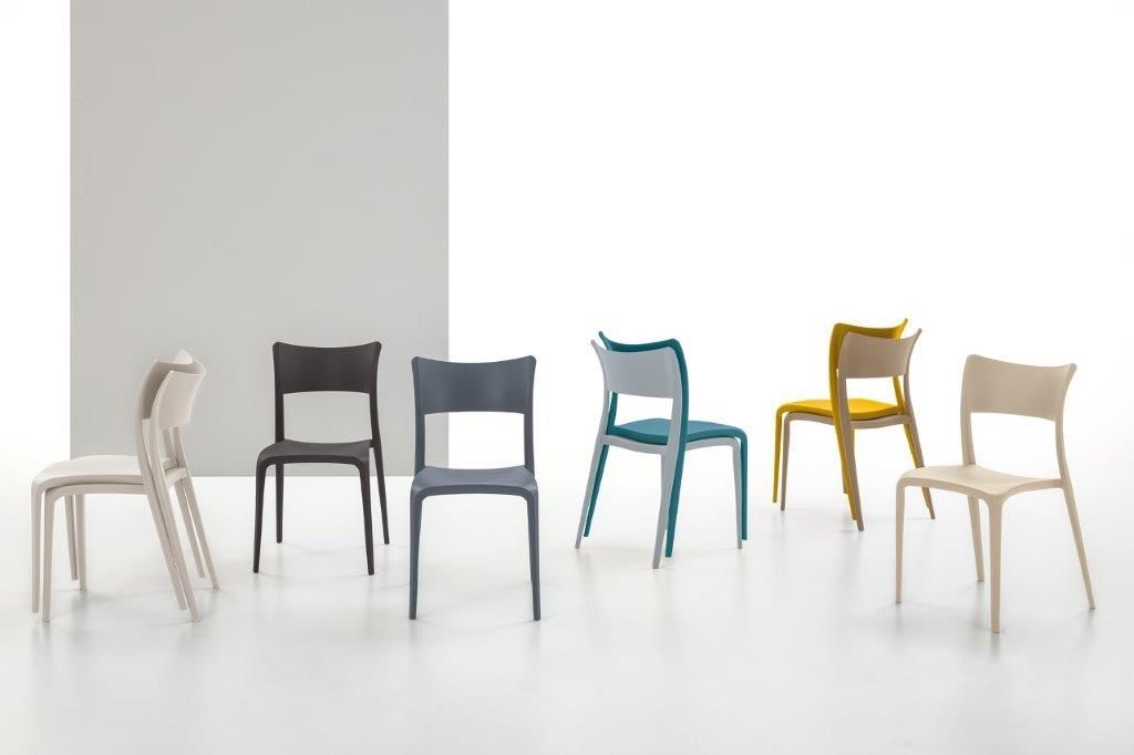 Sei sedie di plastica colorate su uno sfondo bianco; diverse tonalità di grigio, verde acqua e giallo.