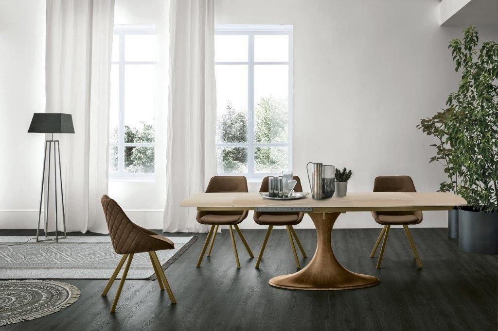 Sala da pranzo con tavolo in legno, sedie marroni e lampada da terra vicino a una finestra.