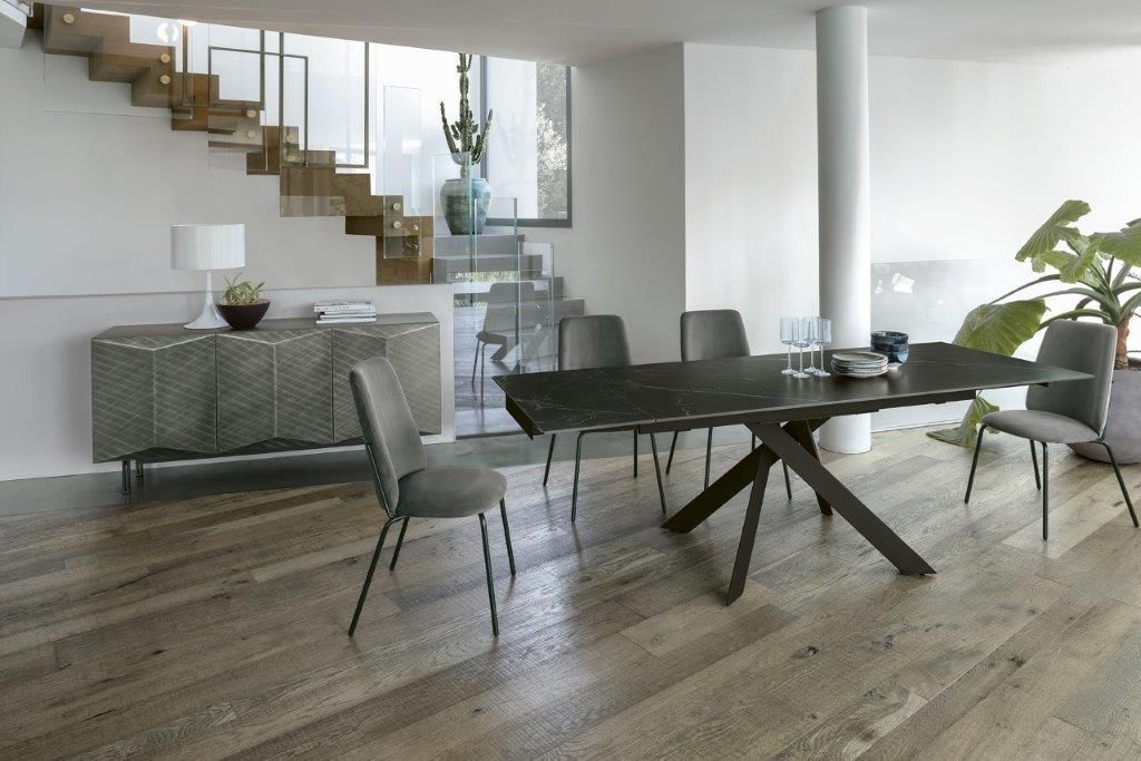 Sala da pranzo con pavimento in legno, tavolo, sedie, scale e buffet decorativo.